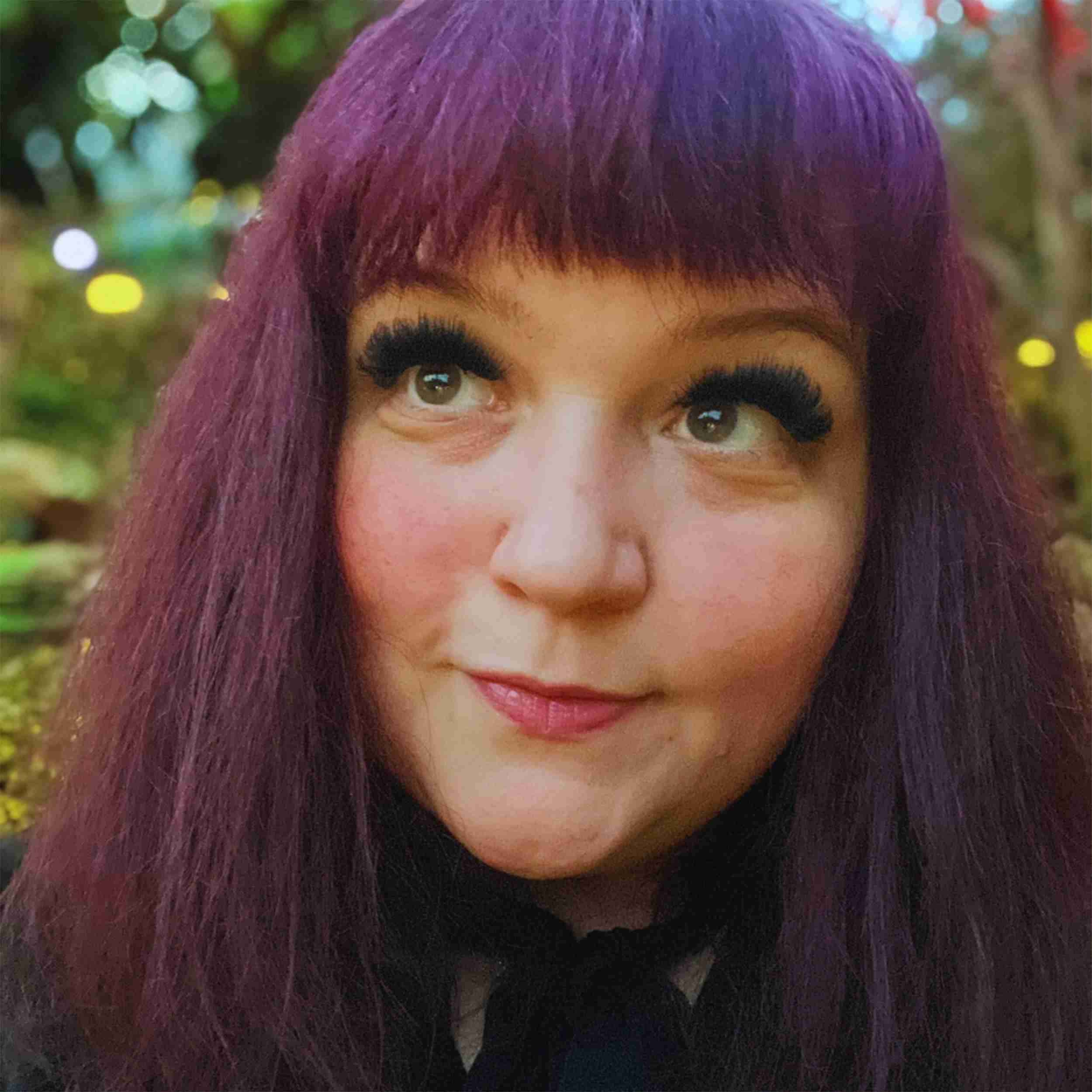 A person with purple hair looking upwards with a slight smile. A person with purple hair looking upwards with a slight smile.
